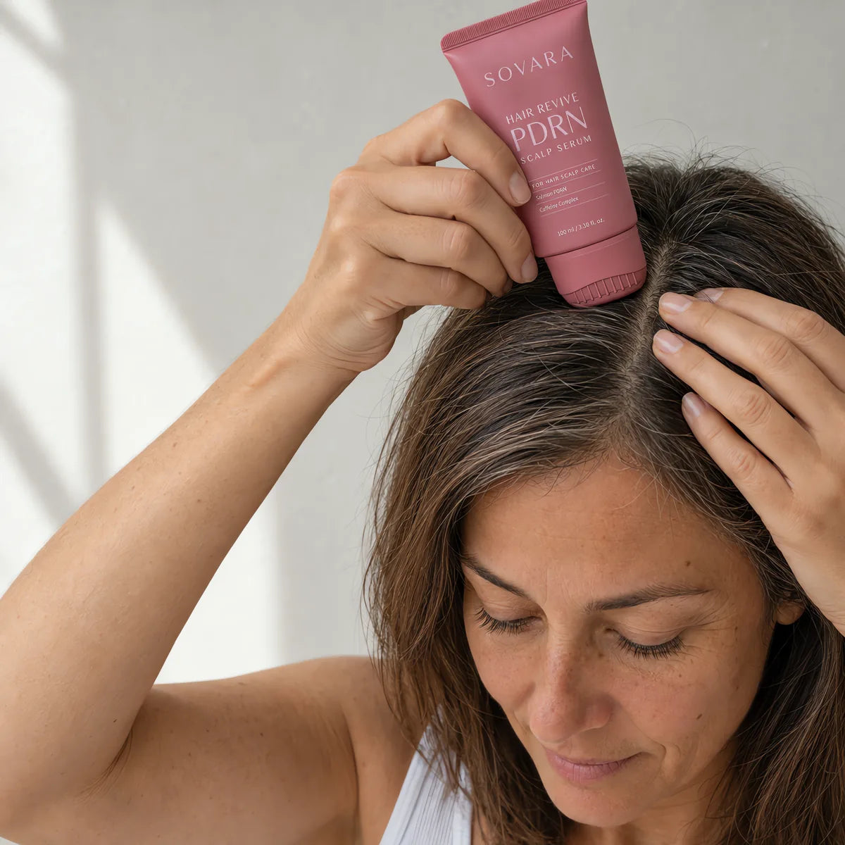A woman putting the Sovara scalp serum on her part line